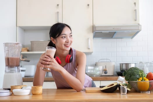 A healthy young woman in a modern kitchen making a nutritious juice using fresh vegetables and fruits, smiling and enjoying the process.