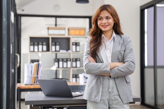 A confident young businesswoman stands at her desk, exuding professionalism in a modern office environment.