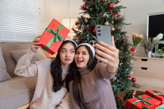 Young female couple enjoying a Christmas party, taking selfies with gifts and festive decorations.
