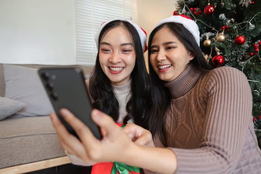 Happy young women celebrating Christmas with gifts and festive decorations, capturing joyful moments in a cozy home environment.