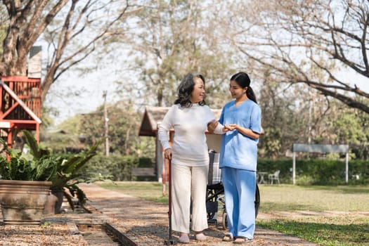 An elderly woman is being helped by a caregiver during her rehabilitation in a serene outdoor park environment.