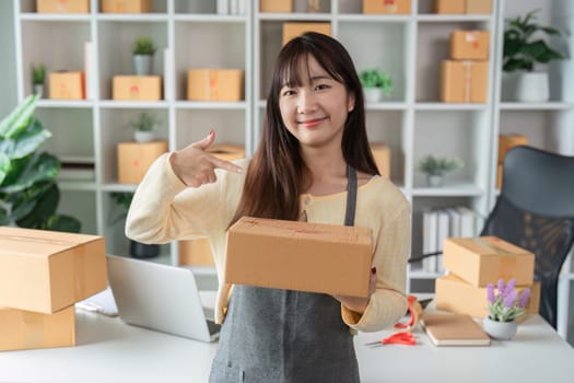 A cute woman in a modern home office taking online sales orders, surrounded by shipping boxes and a laptop, showcasing e-commerce business.