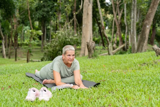 Elderly woman enjoying yoga and stretching exercises outdoors, promoting health and wellness in a serene park environment.