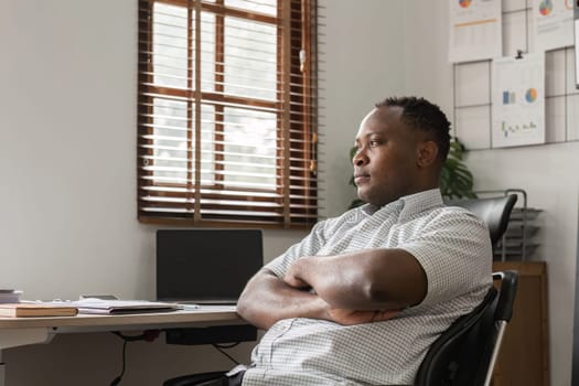 A male office worker sits at his desk, appearing stressed and deep in thought, surrounded by office equipment and charts.
