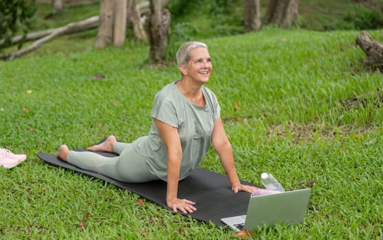 Elderly woman practicing yoga and stretching in a garden, emphasizing health, fitness, and an active lifestyle in a serene outdoor environment.