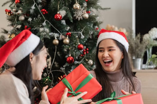 Happy young women exchanging gifts by the Christmas tree, capturing the joy and excitement of the holiday season.