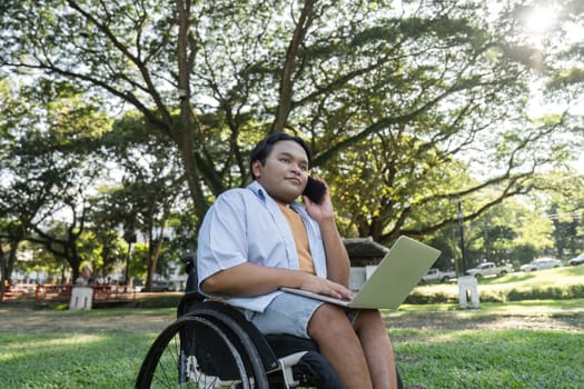 A young man in a wheelchair uses a laptop while sitting in a sunny park, showcasing accessibility and remote work.