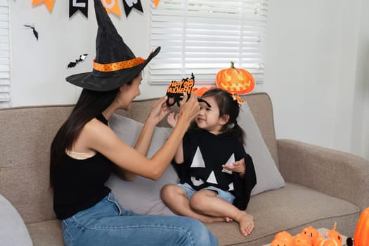 A loving mother and her daughter dress up in Halloween costumes and joyfully decorate their living room with festive Halloween decorations.