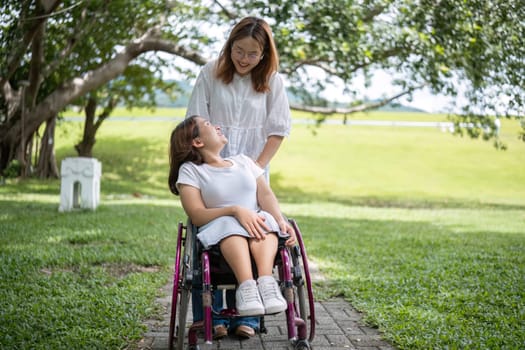 A young woman in a wheelchair and her best friend share a joyful moment walking through a lush green park.