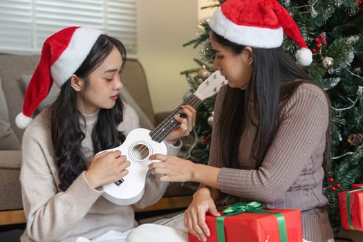 Two young women happily playing music together on Christmas, surrounded by gifts and festive decorations.