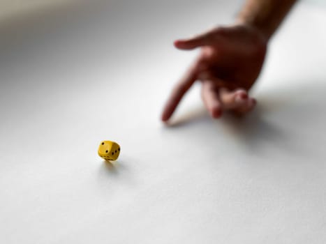 Hand rolling yellow dice on white surface representing chance and risk in game.