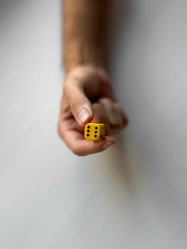 Hand holding yellow die with six dots reflecting chance and game concepts.