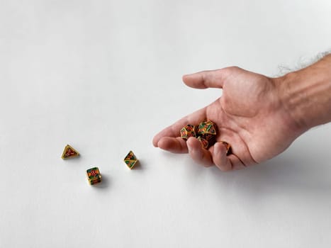 Hand holding colorful polyhedral dice on white surface for tabletop gaming.