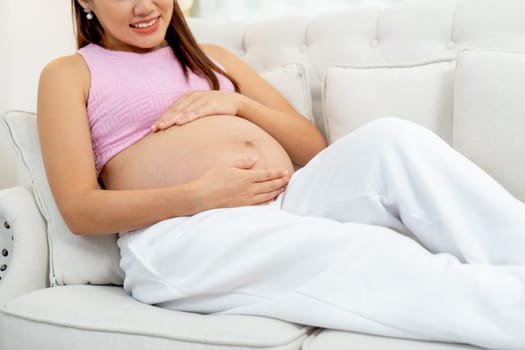 Close up pregnant woman sit and relax on sofa in living room and look happiness with touch her belly.