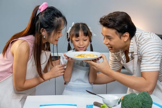 Close up Asian family with father, daughter and pregnant mother hold and look at omelet dish in the kitchen with happiness.