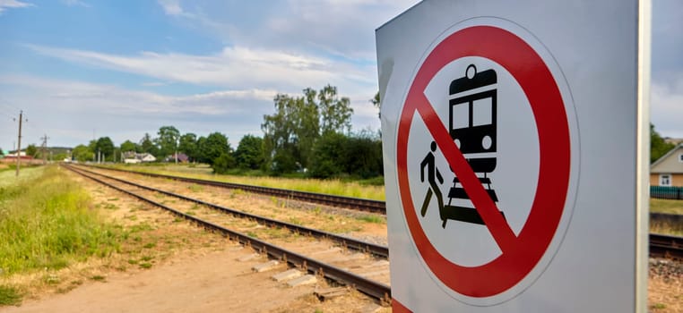 A concrete railway track under a sunny sky with a vivid prohibition sign displaying a train and a person, emphasizing no crossing. The scene captures rail safety on a lovely day.