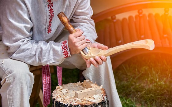 A skilled craftsman, clad in a white shirt adorned with red embroidery, meticulously carves a wooden spoon with a sharp knife. Wood shavings scatter around him, hinting at his dedication and the slow, meticulous process. The warm, natural light creates a sense of focus and tranquility as he works.