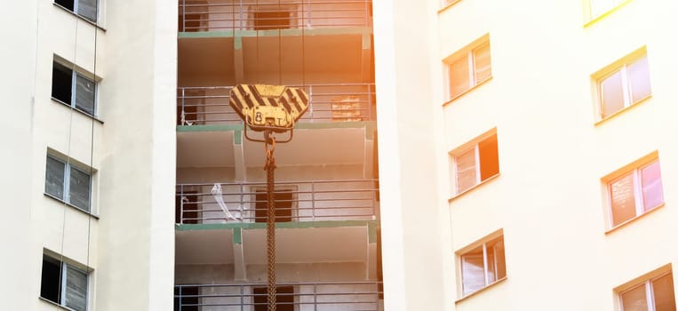 Heavy machinery operates at a residential construction site where a large crane gracefully lowers materials to the upper floors of an urban apartment building. The sun casts a warm glow, illuminating the structure and highlighting the diligent efforts of the construction team.