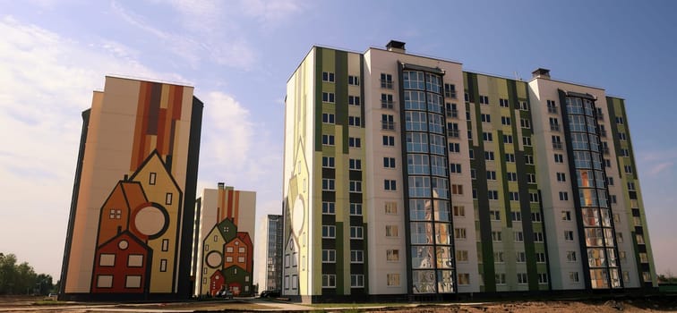 A cluster of modern residential buildings showcases innovative architectural designs with vibrant colors and distinctive patterns. The structures are set against a clear blue sky, emphasizing their contemporary style and urban environment.