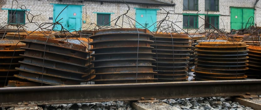 Rusted metal plates are stacked neatly beside railway tracks at an abandoned industrial location on a cloudy day, showcasing signs of wear and disuse.