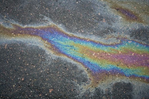 Shimmering gasoline spill produces a vibrant rainbow effect on asphalt, highlighting the issue of environmental pollution.