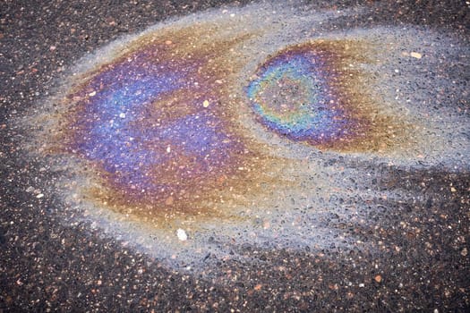 A multi-colored oil or gasoline slick that creates a bright shine on wet asphalt, illustrating the effects of environmental pollution.