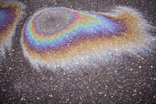 A multi-colored gasoline or oil slick creating a bright shine on wet asphalt, demonstrating environmental problems