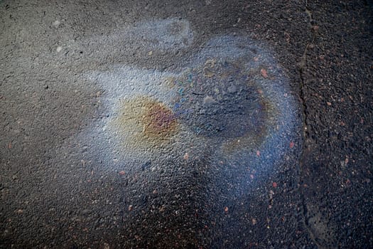 A bright petrol or oil slick creating a colourful sheen on a black asphalt road.