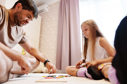 A man and young girl sit on the floor and play with colorful pieces. They are likely engaged in a board game or building blocks.