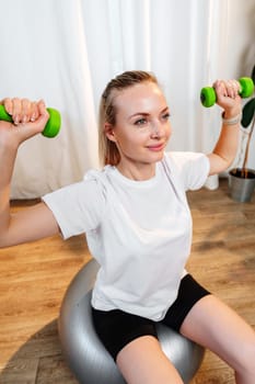 Woman exercising with dumbbells on a stability ball in a bright indoor space