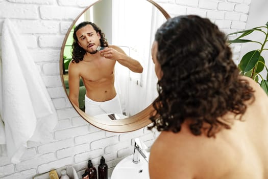 A man with curly hair grooming himself in the bathroom while looking into a round mirror close up