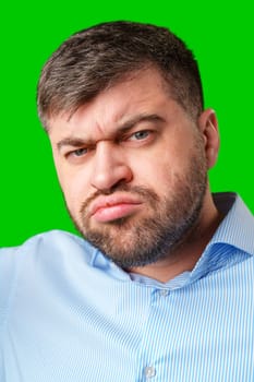 A man with a serious expression wearing a light blue shirt poses against a bright green background in studio