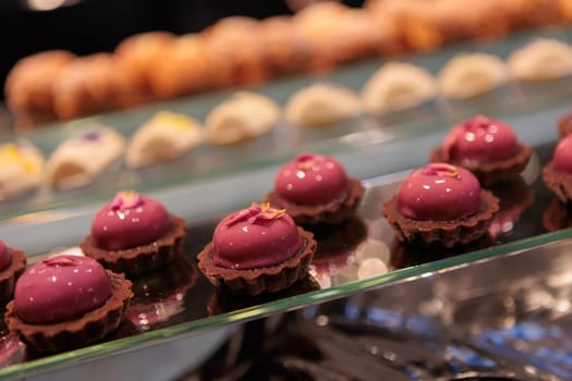 Elegant mousse cakes with a creamy filling and a surprise center of strawberry jam, coated in a smooth pink glaze and sprinkled with freeze-dried raspberry pieces on a crisp biscuit base
