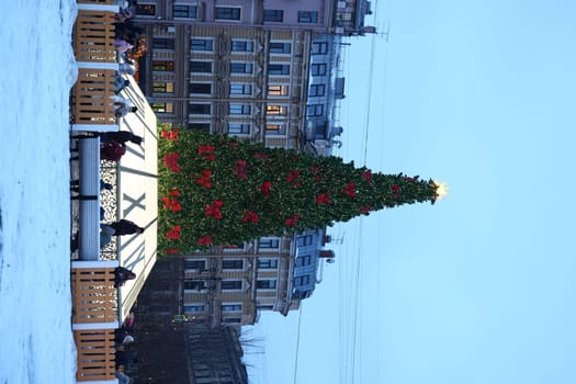 A beautifully decorated Christmas tree stands prominently in a snowy city square, fostering a joyful holiday atmosphere