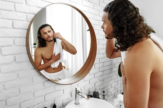 Young man grooming himself in a modern bathroom mirror with natural lighting and minimalistic decor