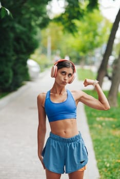 A fit woman confidently flexes her bicep while showcasing her stylish workout attire in a beautiful park setting