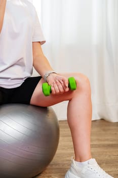 Woman exercising with dumbbells on a stability ball in a bright indoor space