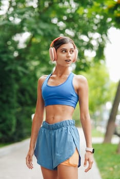 A fit and energetic young woman enjoys jogging outdoors in the park, happily listening to music through her headphones