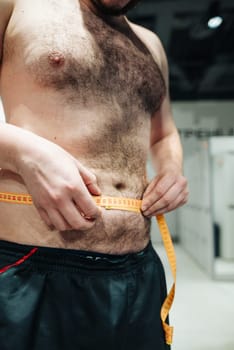 A man is diligently measuring his waist size as a way to effectively track his fitness progress and overall health