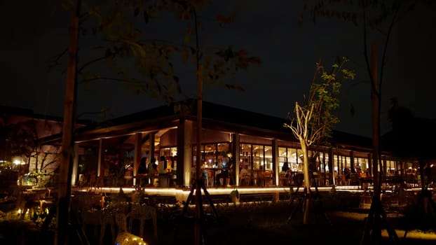 Cozy restaurant exterior at night with warm lighting and silhouettes of people dining inside.