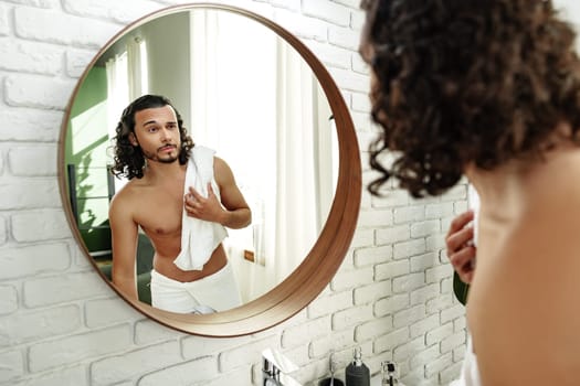 Young man grooming himself in a modern bathroom mirror with natural lighting and minimalistic decor