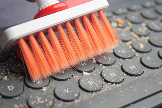 A hand skillfully uses a brush to clean dust and debris from a computer keyboard