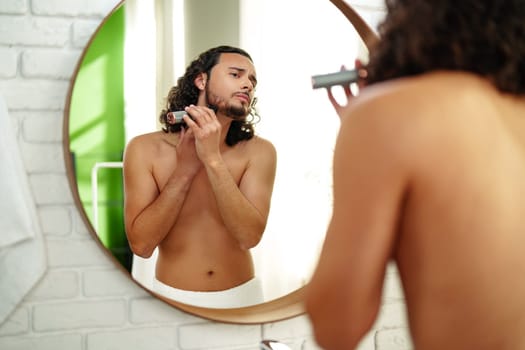 A man with curly hair grooming himself in the bathroom while looking into a round mirror close up