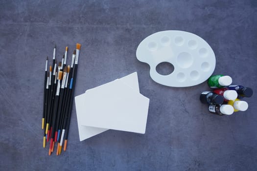 A flat lay displays painting supplies like brushes, a vibrant palette, and blank canvases