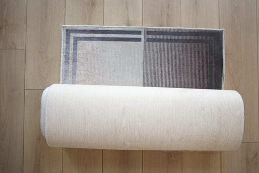 A beautifully designed stylish area rug is currently partially rolled up on a wooden floor