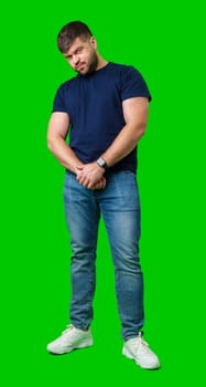 Man standing with a thoughtful expression in a casual outfit against a green background in studio
