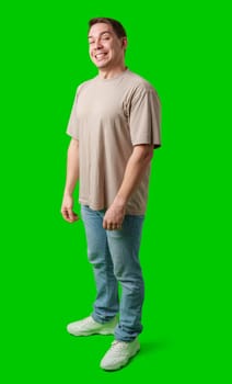 Young man stands confidently in a plain beige t-shirt and jeans against a bright green background in studio