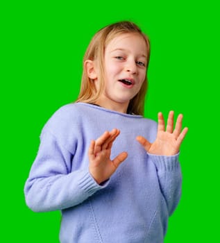A young girl expresses surprise while smiling, with bright green background and cozy sweater