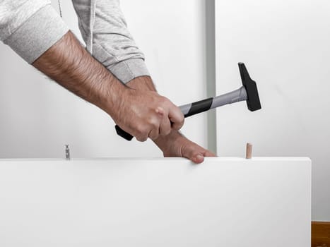 Male adult Caucasian assembling furniture with hammer and wooden pegs.