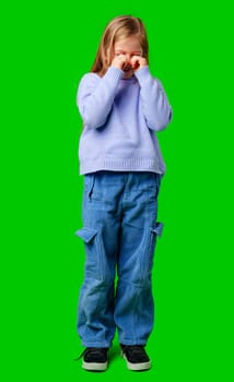 A young girl in a cozy sweater and blue cargo pants expressing emotion with a bright green background in studio